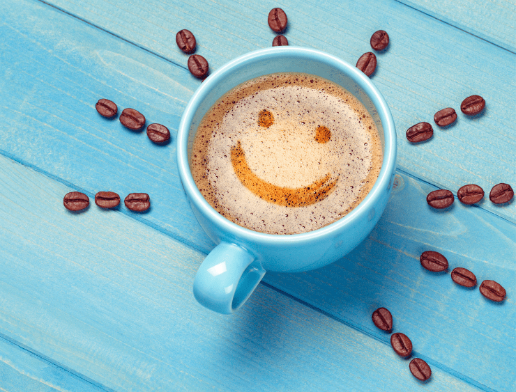 Kaffeetasse mit Smiley auf dem Kaffee und rundherum Kaffeebohnen als Sonnenstrahlen für bessere Laune