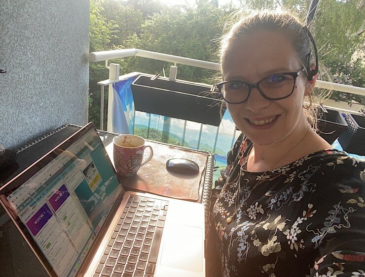 Petra Prinz lächelt in die Kamera und zeigt sich beim Bloggen mit MacBook am Balkon